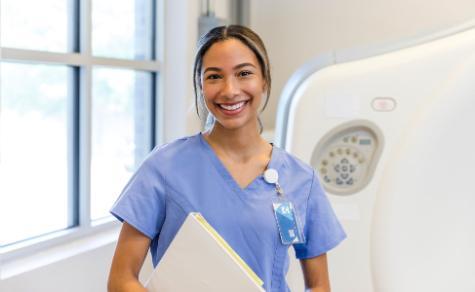 Radiology technician smiling next to CT scan machine