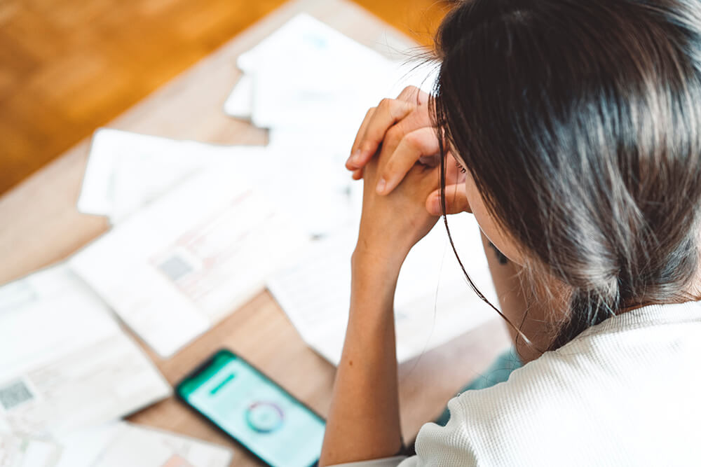 Young woman looking at bills and her smartphone to pay bills and check her finances.