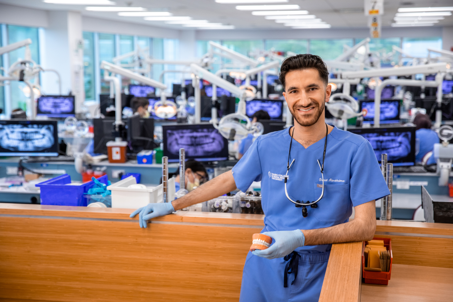 Daniel Abrakhaimov, in scrubs, smiles at the camera in the dental simulation lab.